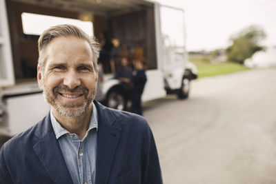 Portrait of happy businessman standing on road with colleagues and portable office truck in background