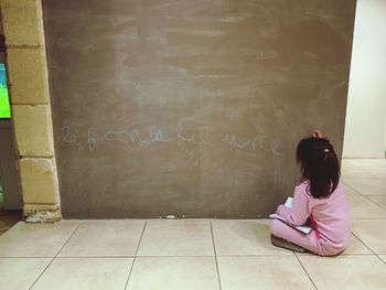 Rear view of woman sitting against wall in building