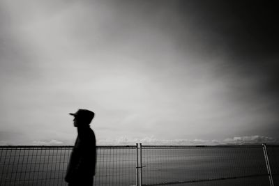 Silhouette woman standing by railing against sea