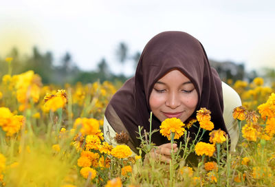 Portrait of young woman with yellow flowers in field