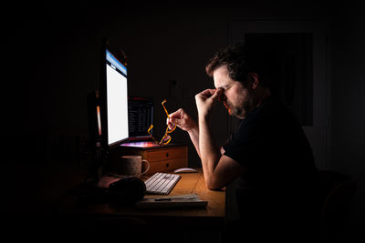 Side view of tired man using laptop at home at night