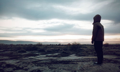 Silhouette of woman standing on landscape against cloudy sky