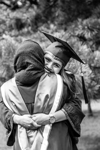 Portrait of woman in graduation gown embracing friends 