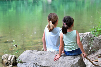 Rear view of women sitting on rock by lake