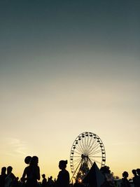Silhouette people at amusement park against clear sky