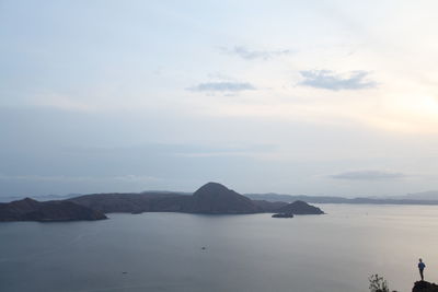 Mid distance view of man standing on cliff by sea against sky