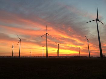 Silhouette windmill on field against orange sky