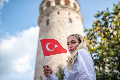 Low angle view of woman holding flag while standing against building