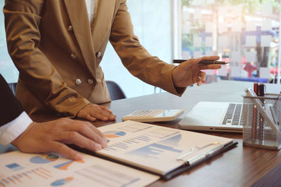 Cropped image businesswoman pointing at laptop while colleague siting at desk