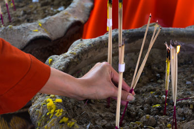 Cropped hand of woman inserting burning incense sticks in soil at temple
