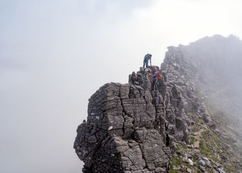 Man helping woman to climb rocky mountain