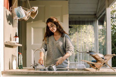 Teenage girl washing utensil in sink outside house