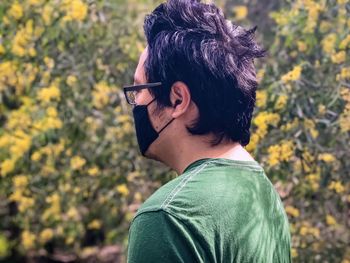 Portrait of young man wearing glasses and face mask against yellow flowering plants.