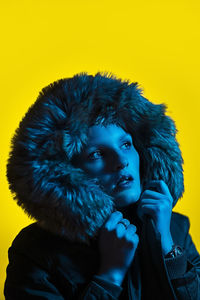 Close-up of woman wearing fur hat looking away while standing against yellow background