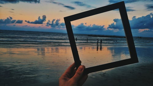 Close-up of hand holding sea against sky at sunset