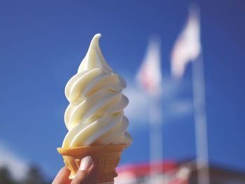 Low angle view of cropped hand holding ice cream against sky
