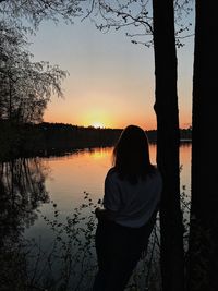 Silhouette woman standing by lake against sky during sunset