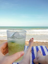 Low section of woman holding drink at beach