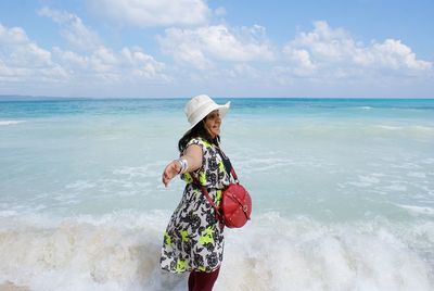 Side view of woman with arms outstretched standing in sea at beach