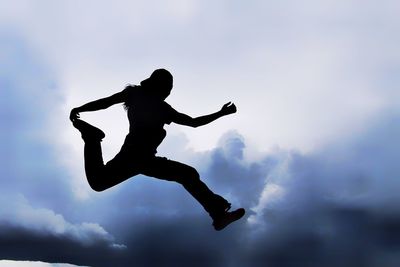 Silhouette of woman leaping against sky