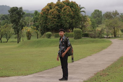 Portrait of young man standing on footpath at park