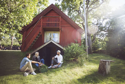 Friends sitting with vegetable crate outside cottage on sunny day