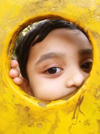 Close-up of boy looking through yellow play equipment at playground