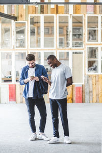 Full length of smiling businessmen text messaging using mobile phones at creative workplace