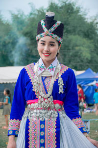 Portrait of smiling young woman in traditional clothing standing on grass against sky