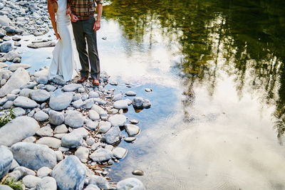 Low section of wedding couple standing on rocks by lake