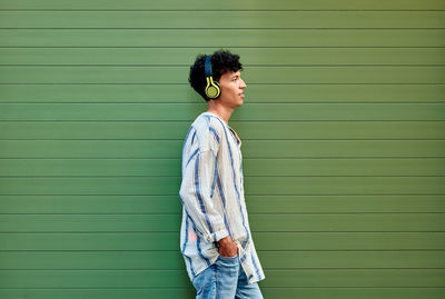 A young afro-haired man listens to music on a green background