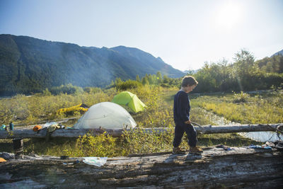 Young boy balancing on fallen log near wilderness campsite, canada.