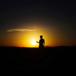 Silhouette man standing on field against sky during sunset