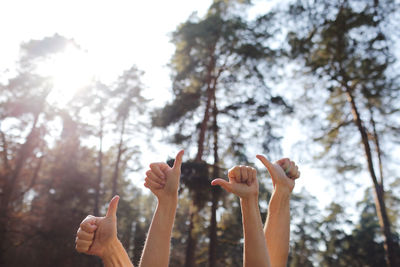 Low angle view of hands showing thumbs up against trees