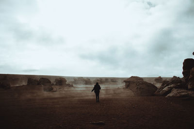 Rear view of woman standing on rock formation against sky