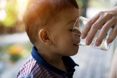 Cropped hand of parent holding glass while boy drinking water