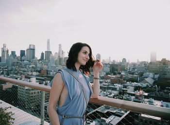 Beautiful woman standing by railing against cityscape