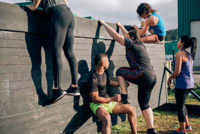 Friends climbing wooden wall while exercising outdoors