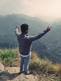 High angle view of man with arms outstretched standing on cliff against sky