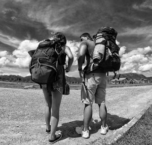 Rear view of friends walking on road against sky