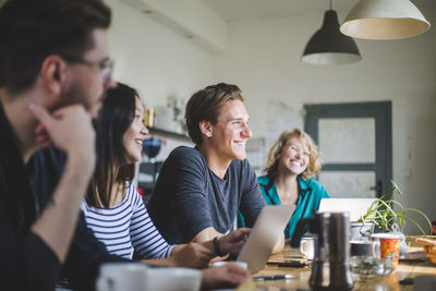 Happy computer programmers looking away while working at table in office