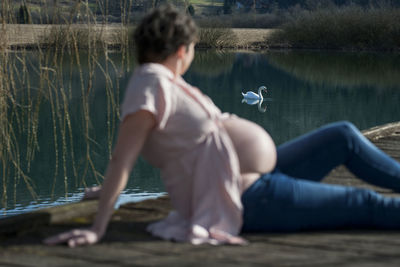 Pregnant woman at lakeshore looking at swan