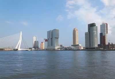 Erasmus bridge and buildings by river against sky