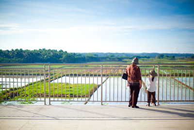 Rear view of people walking in farm against sky