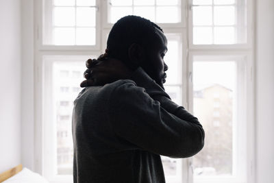 Side view of tired man against window at home