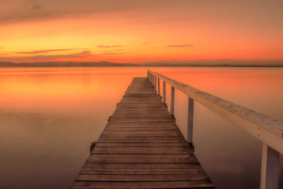 Pier over sea against orange sky