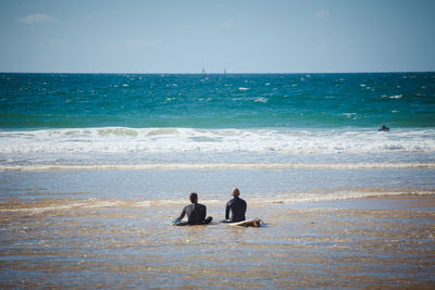 Men sitting on surfboard amidst sea against sky