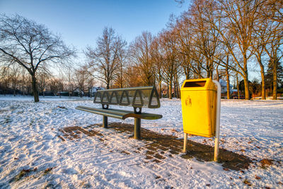 Empty park bench on snow covered field against sky