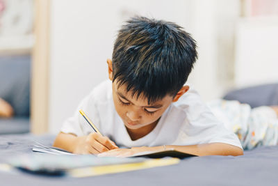 Cute boy writing in book at home