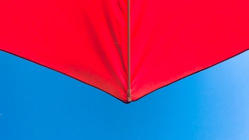 Directly below shot of red umbrella against clear blue sky